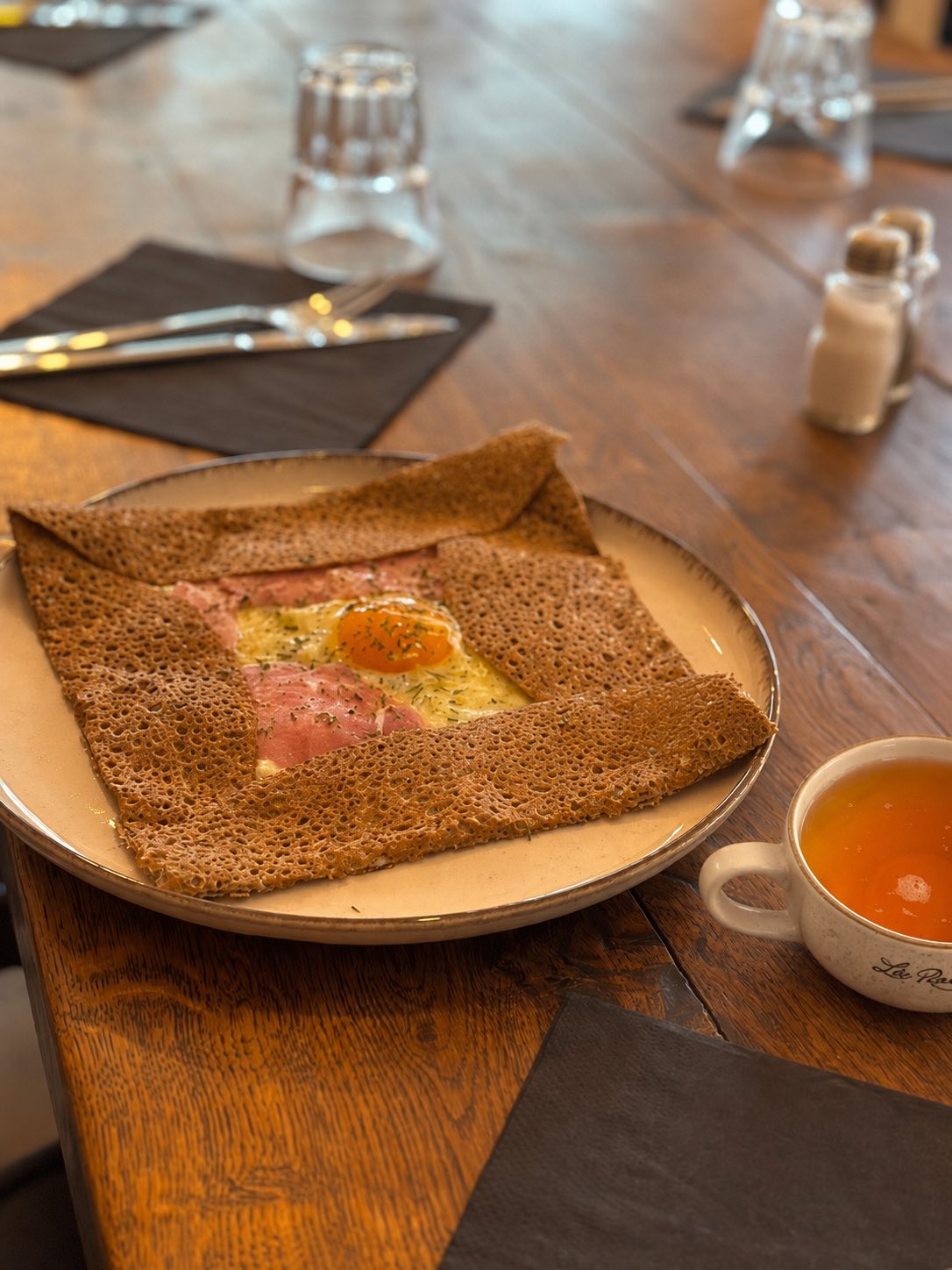 Galette complète œuf jambon fromage servie sur une table en bois avec une bolée de cidre